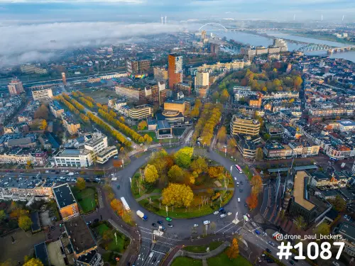 Luchtfoto van de rotonde Keizer Karel Plein in Nijmegen in herfstkleuren, met een mistbank en de Waal op de achtergrond