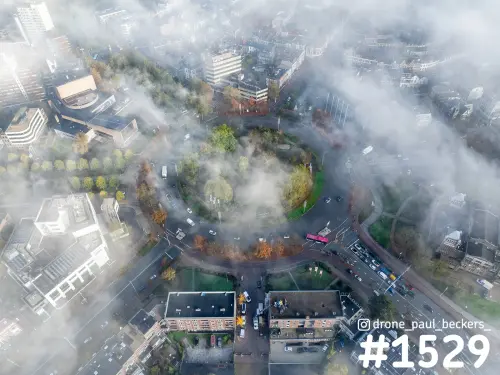 Luchtfoto van het Keizer Karel Plein in Nijmegen met mist tussen de gebouwen en herfstkleuren in de bomen rond de rotonde