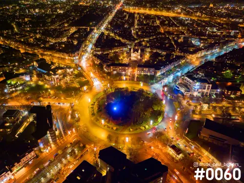Luchtfoto van Keizer Karel Plein in Nijmegen 's avonds, met blauw verlicht plantsoen midden in de oranje verlichte rotonde