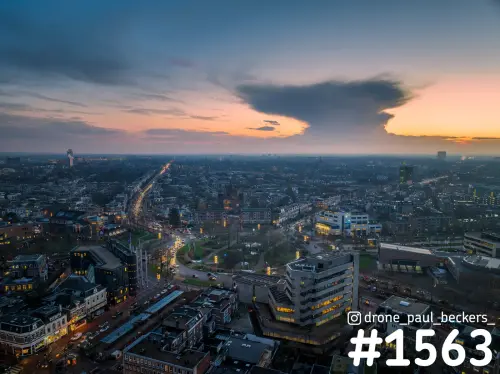 Luchtfoto van Keizer Karel Plein in Nijmegen in de schemering, met verlichte kantoren en een donkere wolk boven de stad