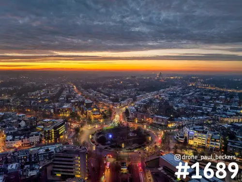 Luchtfoto van het Keizer Karel Plein in Nijmegen na zonsondergang, met verlichte straten en een oranje gloed aan de horizon
