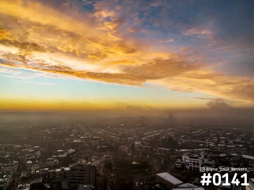 Luchtfoto van Keizer Karel Plein in Nijmegen bij zonsopkomst, met oranje wolken boven een stad vol ochtenddnevel