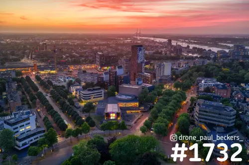 Luchtfoto van Keizer Karelplein in Nijmegen met de Stadsschouwburg en verlichte lanen onder een roodoranje avondlucht