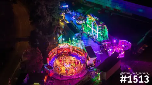 Luchtfoto van de kermis in Nijmegen bij nacht met felgekleurde neonverlichting rond een draaiende attractie bij het Valkhof