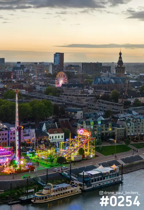 Luchtfoto van de kermis aan de Waal in Nijmegen in de schemering, met reuzenrad en de toren van de Stevenskerk
