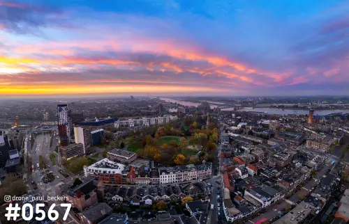 Luchtfoto van Nijmegen met het Kronenburgerpark in herfstkleuren onder een roze en oranje wolkenlucht, Waal aan de horizon