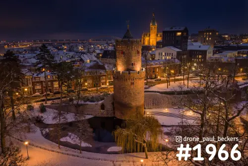 Luchtfoto van de ronde toren in het Kronenburgerpark, Nijmegen, in de sneeuw met Stevenskerk en Waalbrug bij avondlicht