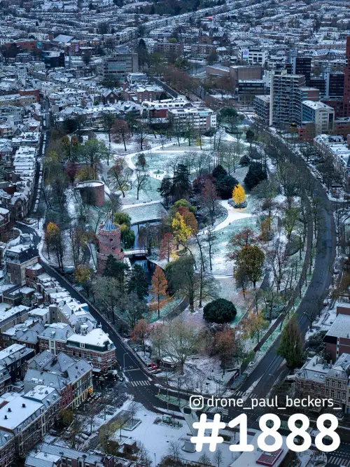 Luchtfoto van het Kronenburgerpark in Nijmegen met een laagje sneeuw en gele herfstbladeren, bij een ronde stenen toren