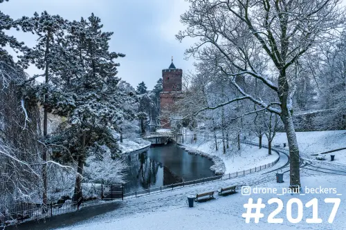 Besneeuwd Kronenburgerpark in Nijmegen met bakstenen toren, vijver en bankjes onder bomen met rijp in winterlicht