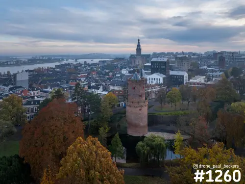 Luchtfoto van de ronde stenen toren in het Kronenburgerpark in Nijmegen, met herfstbomen en de Stevenskerk en Waal op de achtergrond