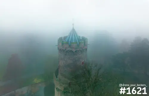 Luchtfoto van een ronde bakstenen toren met blauwgroen dak in het Kronenburgerpark in Nijmegen, gehuld in dikke mist