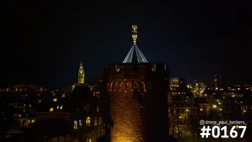Luchtfoto van een verlichte bakstenen toren in het Kronenburgerpark in Nijmegen bij nacht, met de Stevenskerk erachter