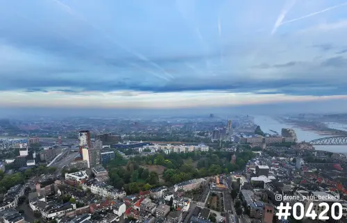 Luchtfoto van Kronenburgerpark in Nijmegen met de Waal rechts en een wolkenlucht met condensstrepen boven de stad