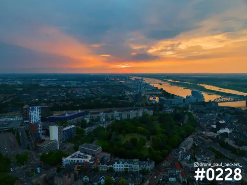 Luchtfoto van Nijmegen bij zonsondergang met het Kronenburgerpark, de Waal en een oranje lucht met donkere wolken