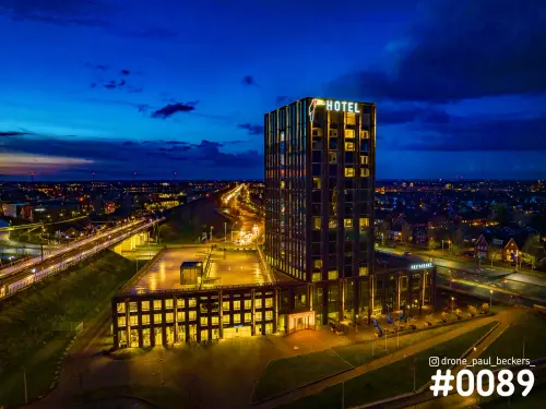 Luchtfoto van een verlicht hotel met restaurant in Nijmegen-Lent in de avondschemering, met een blauwe lucht en verkeer op de weg