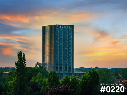 Hoogbouw met hotel in Nijmegen-Lent bij zonsondergang, met oranje en blauwe wolken boven de bomen