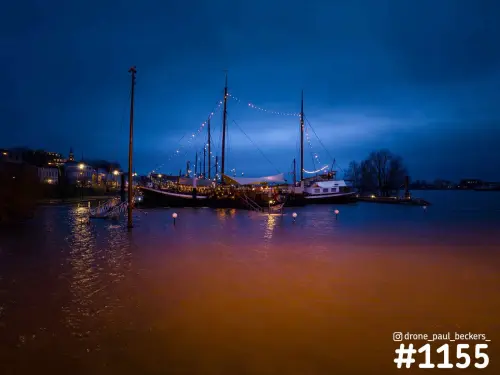 Schepen met masten en lichtslingers in de Lindenberghaven in Nijmegen, blauwe avondlucht en oranje spiegeling in het water