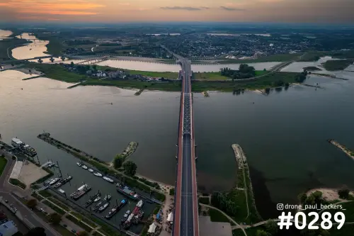 Luchtfoto van de Lindenberghaven in Nijmegen met afgemeerde boten naast een brug over de Waal in het schemerlicht