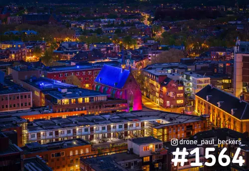 Luchtfoto van de Marienburg kapel in Nijmegen in de avond, blauw en paars uitgelicht tussen verlichte daken van het centrum