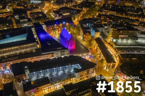 Luchtfoto van de Marienburg kapel in het centrum van Nijmegen 's avonds, blauw en roze verlicht tussen daken en verlichte straten