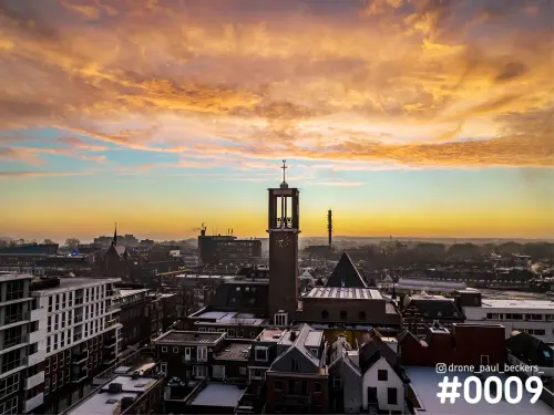 Luchtfoto van de Marienburg kapel in Nijmegen met klokkentoren en kruis, onder een oranje wolkenlucht in het gouden uur
