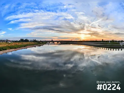 Luchtfoto van de nevengeul bij De Oversteek in Nijmegen, met wolken die weerspiegelen in het water bij zonsondergang
