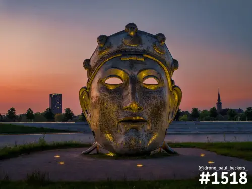 Groot metalen beeld van een gezicht met gouden ogen bij de Nevengeul in Nijmegen-Lent, met roze avondlucht erachter