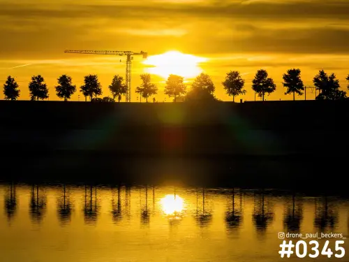Gouden zon boven de Nevengeul in Nijmegen-Lent, met bouwkraan en bomen als silhouet en weerspiegeling in het water