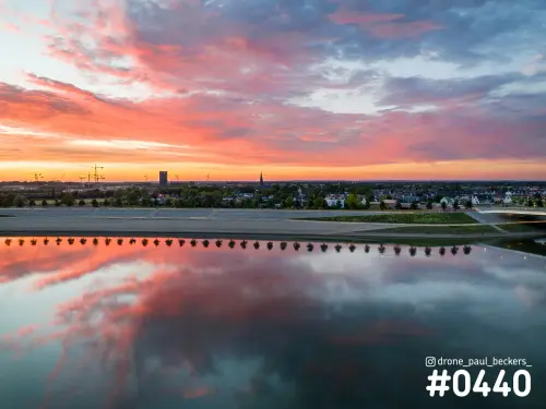 Luchtfoto van de nevengeul bij Nijmegen-Lent in schemering, roze wolken en een rij bomen spiegelen in het water