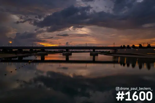 Brug over de Nevengeul in Nijmegen-Lent bij schemering, met donkere wolken en oranje nagloed weerspiegeld in het water