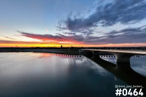 Luchtfoto van de Nevengeul in Nijmegen in de schemering, met brug en een rode wolkenlucht weerspiegeld in het water