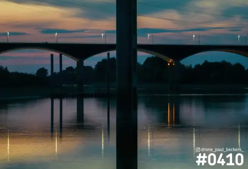 Brug met betonnen bogen over de Nevengeul in Nijmegen bij schemering, met lichtjes die weerkaatsen in het water