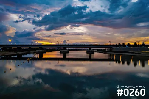Brug over de Nevengeul in Nijmegen bij zonsondergang, met dramatische wolken en hun spiegeling in het stille water
