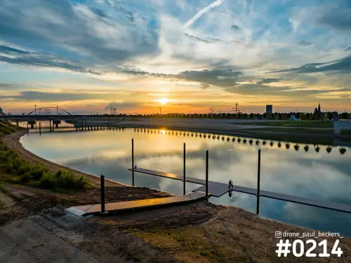 Nevengeul in Nijmegen bij zonsondergang, met steigers op het stille water en De Oversteek als boogbrug in de verte
