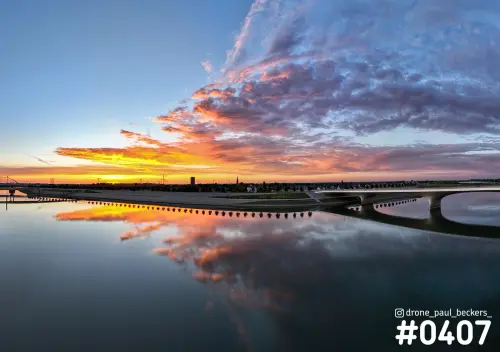 Luchtfoto van de Nevengeul bij Nijmegen met een gekleurde wolkenlucht die weerspiegelt in het stille water, met een brug rechts