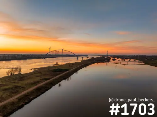 Luchtfoto van de Nevengeul en De Oversteek over de Waal bij Nijmegen, met oranje lucht en windmolens aan de horizon