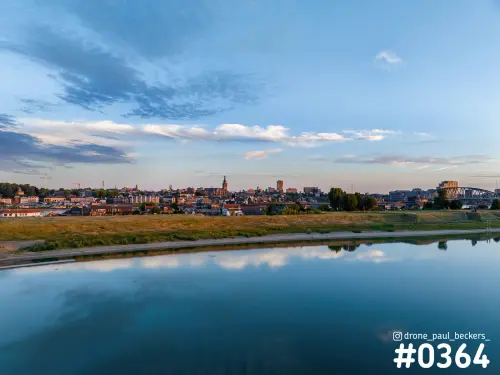 Luchtfoto van de Nevengeul bij Nijmegen in avondlicht, met wolken weerspiegeld in het stille water en de stad aan de horizon