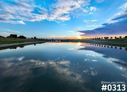 Nevengeul bij Nijmegen bij zonsondergang, met wolken die spiegelen in het stille water en een brug aan de horizon