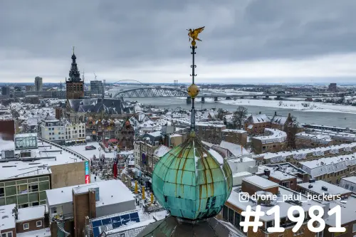 Luchtfoto van het besneeuwde centrum van Nijmegen met groene torenkoepel, Stevenskerk en de Waal op de achtergrond
