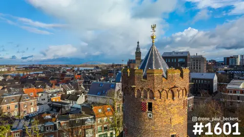 Luchtfoto van een ronde bakstenen stadstoren in Nijmegen, met Stevenskerk en Waalbrug op de achtergrond in winterlicht