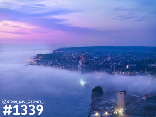 Luchtfoto van het centrum van Nijmegen in de schemering, met mist boven de Waal en roze en paarse wolken boven de stad