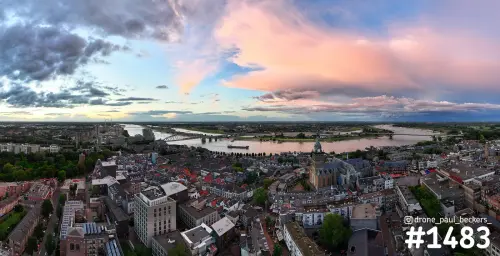Panorama van het centrum van Nijmegen met de Stevenskerk, de Waal en de Waalbrug onder roze en grijze wolken bij zonsondergang