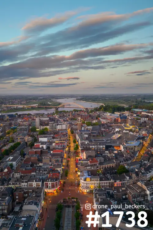 Luchtfoto van het centrum van Nijmegen in de schemering, met verlichte straat en de Waalbrug in de verte aan de Waal