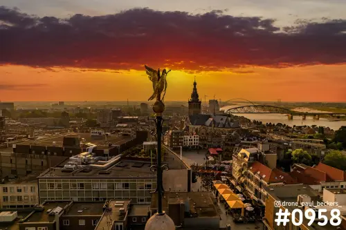 Nijmegen centrum bij zonsondergang met gouden gevleugeld beeld op de voorgrond, kerktoren en De Oversteek over de Waal