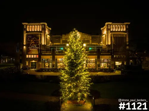 Luchtfoto van een verlicht gebouw met twee torens en een grote kerstboom met lichtjes op het plein in Nijmegen bij avond