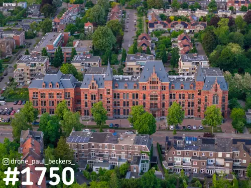 Luchtfoto van een groot rood bakstenen gebouw met grijze leistenen daken en torentjes in Nijmegen-Oost, omgeven door bomen