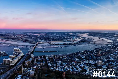 Luchtfoto van Nijmegen en de Waal in de schemering, met bruggen, roze horizon en winterse daken in het centrum