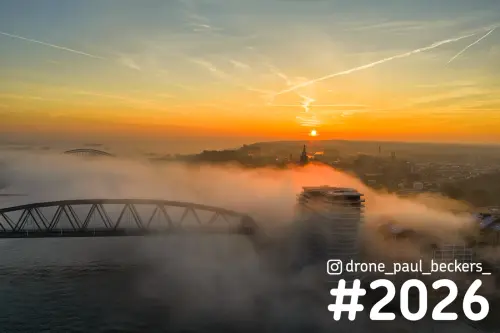 Luchtfoto van Nijmegen bij zonsopkomst met mist boven de Waal, een stalen brug en de toren van de Stevenskerk