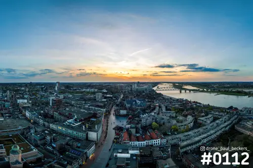 Luchtfoto van Nijmegen bij zonsondergang met de Waal, De Oversteek in de verte en de Stevenskerk tussen de daken