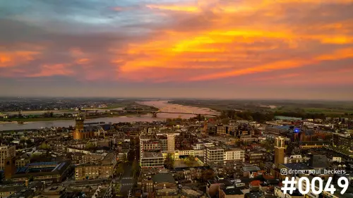 Luchtfoto van Nijmegen bij zonsondergang, met de Waal, de Waalbrug en de Stevenskerk onder een oranjerode wolkenlucht